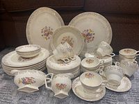 Photo showing full set of dinner plates, cups, bowls, and serving platters with floral pattern and 22k gold trim.