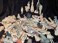 Photo showing Victorian paper dolls including adult, child, baby and nanny figures with numerous paper clothing pieces spread out on a black background.