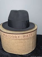 Full view of black vintage Mallory fedora hat displayed on its original branded Mallory Hats box showing the hat style and grosgrain band details.