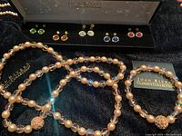 Joan Rivers Classics Collection earrings in multiple colors displayed in black jewelry box; beaded faux pearl and crystal necklace and bracelet laid out with branded velvet pouch and vase