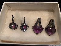 Both pairs of vintage earrings displayed in a box on a soft white cushion.