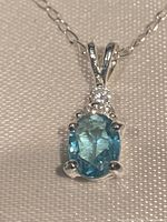 Close-up photo of the pendant showing the oval blue gemstone and clear stone above it.