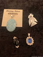 Four pieces of vintage jewelry on a black surface: a large blue semi-precious stone pendant on a card, a mother of pearl bird pin, a black stone pendant, and a blue stone pendant with clear stones.
