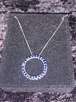 Full view of the pendant necklace on black velvet background showing the entire circle pendant with sapphires and chain.