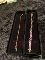 Side by side view of both vintage tennis bracelets in black display trays showing clasp and stone details.