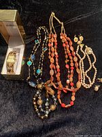 Wide shot of all jewelry items laid out including necklaces, earrings, ring, and Embassy watch in box