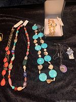 Photo showing several colorful bead necklaces, a stone wrap bracelet watch in a box, and a Lotus Jade pendant necklace with a purple lotus symbol.