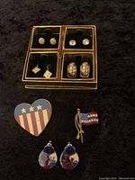 Photo of vintage jewelry lot showing Nolan Miller Glamour Collection gold-tone rhinestone earrings in gold-tone box, enamel floral drop earrings, and two USA flag pins.