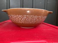 Side view of the Vintage Pyrex Woodland 444 Cinderella mixing bowl showing brown exterior with white floral pattern and handles.