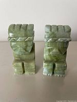 Front view showing two small green jade figurines with stylized faces and geometric carvings