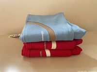 Stack of folded track pants: one light blue with beige and white accents, two red with white bands, brand name visible Nice+Smooth