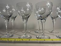 Eight clear tall wine glasses arranged in two rows with a measuring tape showing approximately 7.75 inches height.