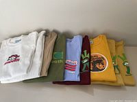Nine women's medium tops and t-shirts folded side by side showing colors and prints