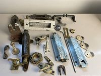A collection of antique metal hardware items including door handles, plates, hooks, locks, and a letter box, all laid out on a white surface.