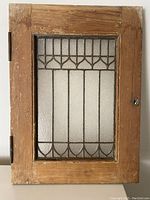 Front view of antique wooden framed leaded glass window with hinges and latch, showing geometric pointed arch pattern in textured glass.