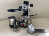 Main unit with portafilter attached on base, milk pitcher, filter basket and aluminum filter assembly placed in front