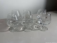 Six clear glass cognac glasses displayed on a flat surface, four smaller glasses in the back and two larger in front right.