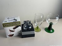 Vinoglobe wine decanter inside original box with two wine glasses beside it, displayed against a neutral background.