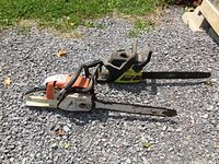 Photo showing two chainsaws lying on gravel; one Stihl with orange and white coloring and one Poulan with yellow and black coloring.
