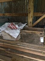 Wooden crate with black lettering 'Auto Knitter Hosiery Co. Toronto' placed on wooden pallets with grain bags beside it in a storage area.