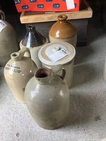 Front view showing all stoneware jugs and the crock with lid arranged in a group on a concrete floor.