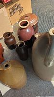 Seven crocks arranged on floor, showing large beige and multiple brown glazed pieces