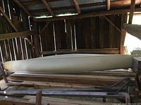 Side exterior view of an off-white fiberglass canoe stored in a barn on wooden supports