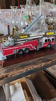 Angle showing full side view of the detailed red and white fire truck model with ladder and platform labeled 'TOWER 1', mounted on a wooden base.