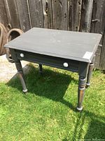 Full view of vintage painted pine table showing distressed paint and scuffs, standing on grass outdoors against a wooden fence.