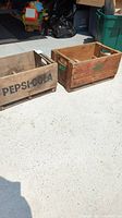 Two vintage wooden crates placed side by side outside; left crate labeled Pepsi-Cola and right crate labeled Muskoka Dry Ginger Ale