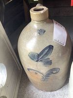 Front view of large pottery jug showing painted floral motif and chips at mouth.