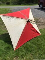 Red and white canvas umbrella laid on grass, showing fabric dirt and condition.
