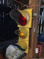 Front side view showing all three lenses (red, amber, green) mounted vertically with yellow metal housing and sun visors, attached to wooden post.