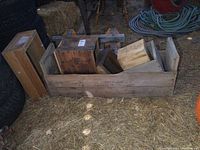Wide view of several old wooden crates arranged inside a large crate, placed on straw ground with tires and hoses nearby.