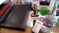 Photo showing the black leather folder with visible wear, amethyst clusters, green glass paperweight sphere, metal figurine, glass Christmas tree, and candle holder.