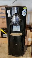 Front view of the black atmospheric water generator machine, showing the dispensing area and control panel.