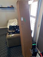 Tall rectangular cardboard box containing wooden bed slats, box standing vertically in room.