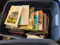 Top-down view of the blue plastic container filled with various paperback and hardcover books.