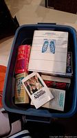 Blue plastic bin filled with six books including a red Life-Mates book, spiral-bound Essentials of Human Anatomy and Physiology, and The Pocket Aquinas.