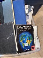 Bin containing assorted books with visible titles such as "Human Race Get Off Your Knees" by David Icke and several other books in black and blue covers.