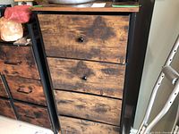 Front view of cabinet showing wood-look cloth coated drawers and metal frame. Three round knobs present, two missing.