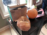 Photo of a pink Himalayan salt candle holder with three tea light candles and a round pink Himalayan salt lamp on a black cabinet.