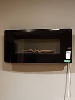 Front view of the black wall-mounted electric fireplace on a wall with visible sticker label.