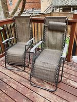 Two brownish-gray woven mesh reclining garden chairs with black metal frames shown upright on a wood deck with scratches.