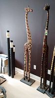 Full view of the tall wooden giraffe sculpture standing upright against a wall, showing its height and feature details including circular cut-outs on body