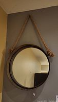 Front view of the round metal framed hanging mirror with rope hanger, showing the distressed finish and clear reflective surface.