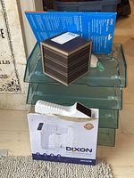 Photo showing four transparent plastic stackable organizers, brown leather-like storage box, and boxed Dixon cordless disinfectant sprayer on floor.