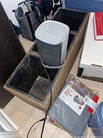 Wicker wood planter with three black square pots, Mibote heater on top, and packaged tree storage bags on floor nearby.