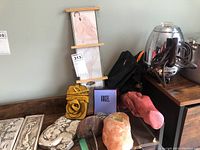 Overview of the lot showing prints, wallet, waist packs, candles, plaster art decor, perfume, and metal wall sconce on wooden furniture.