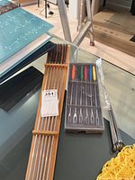 Photo showing metal skewers with wooden handles arranged in wooden holder next to boxed fondue forks with colorful handles on glass table surface.